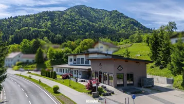 Gebäudeensemble mit moderner Architektur und umliegender Natur vor einer bewaldeten Bergkulisse.