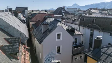 Luftaufnahme eines Gebäudes in einer städtischen Umgebung mit Blick auf die umliegenden Dächer und Berge.