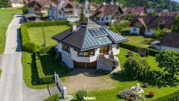 Luftaufnahme eines Hauses mit markanter Dachform und gepflegtem Garten in ländlicher Umgebung.