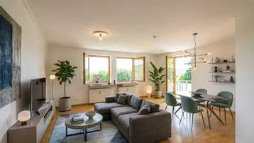 Helles Wohn-Esszimmer mit modernem Sofa, Esstisch und Zugang zu einem Balkon mit grüner Aussicht.