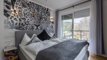 Geräumiges Schlafzimmer mit Leoparden-Wandbild und Balkonzugang mit Blick auf die Hügel.