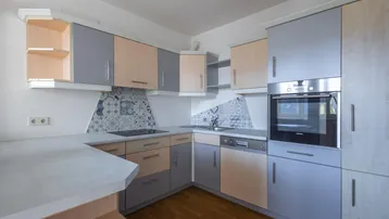 Funktionale Küche mit hellgrauen und holzfarbenen Schränken, ausgestattet mit modernen Geräten und gemusterten Fliesen.