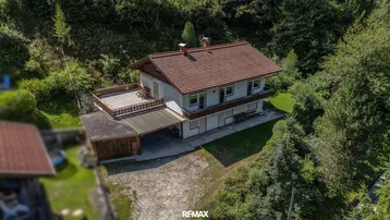 Luftaufnahme eines Einfamilienhauses mit Satteldach, umgeben von üppiger grüner Natur und Bäumen.