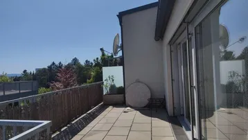 Geräumige Terrasse mit Fliesenboden und Blick ins Grüne unter strahlend blauem Himmel.