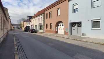 Straße mit mehreren Gebäuden und einem hellblauen Haus unter blauem Himmel.