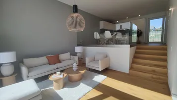 Gemütliches Wohnzimmer mit Sofa, Holzboden und offener Verbindung zum Essbereich über Stufen.