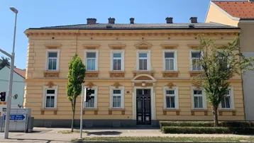 Historisches Gebäude mit gelber Fassade, vielen Fenstern und dekorativen Elementen an einem sonnigen Tag.