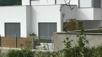 Moderne weiße Fassade eines Gebäudes mit großen Fenstern und Rollläden.