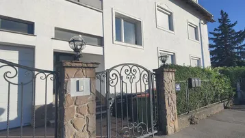 Weißes Wohnhaus mit Steinfassade, schmiedeeisernem Tor und gepflegter Hecke im Vorgarten.