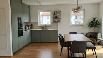 Helle, offene Küche mit modernen grünen Schränken und Essbereich, ausgestattet mit Holzboden und viel Tageslicht.