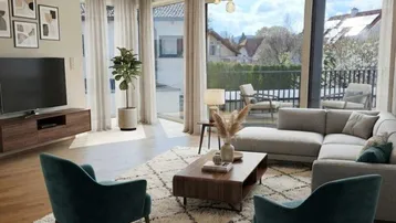 Helles, modernes Wohnzimmer mit Holzboden, großen Fenstern und Zugang zum Balkon mit Blick ins Grüne.