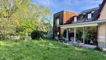 Weitläufiger Gartenbereich neben dem Haus mit moderner Glaserweiterung und Holzfassade.