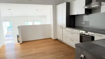 Moderne Küche mit hellen Schränken, dunkler Arbeitsplatte und Holzboden, offen zu einem weiteren Wohnbereich.