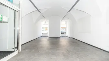 Heller, leerer Geschäftsraum mit gewölbter Decke und großflächigen Fenstern zur Straße.
