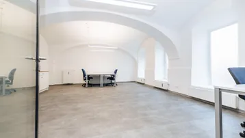 Helles, geräumiges Büro mit hohen Gewölbedecken, großen Fenstern und modernem Fliesenboden.