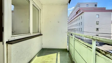 Schmaler Balkon mit grünem Boden und Blick auf die umliegenden Gebäude.