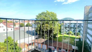 Sonniger Balkon mit Holzboden und Blick auf die Umgebung und grüne Hügel.