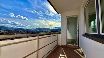 Geräumiger Balkon mit Fliesenboden und weitem Blick auf die umliegende Berglandschaft unter blauem Himmel.