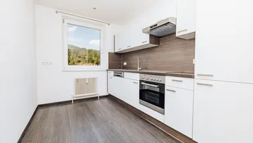 Moderne Einbauküche mit weißen Schränken, dunkler Arbeitsplatte und Fenster mit Bergblick.