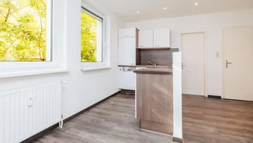 Helle Küche mit weißen Schränken, integrierten Geräten und Blick ins Grüne durch die Fenster.