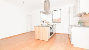 Helle, offene Küche mit Kochinsel, modernen Geräten und hellem Laminatboden.