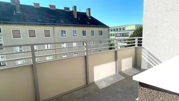Sonniger Balkon mit Fliesenboden und Blick auf die umliegenden Gebäude unter blauem Himmel.