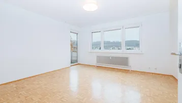 Helles Zimmer mit Parkettboden und Zugang zu einem kleinen Balkon, bietet einen weiten Blick.