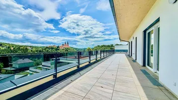 Große, geflieste Terrasse mit Glasgeländer und weitem Blick auf die umliegende Landschaft und ein historisches Gebäude.