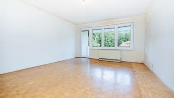 Helles, leeres Zimmer mit Parkettboden, großem Fenster und Zugang zu einem Balkon.