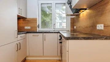 Moderne Küche mit hellen Schränken, Holzoptik-Rückwand und dunkler Arbeitsplatte, gut beleuchtet.