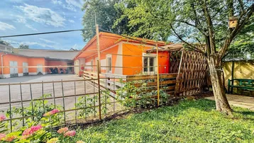 Orangefarbenes Gebäude mit umzäuntem Gartenbereich, Pflanzen und einem Vogelhaus im Baum.