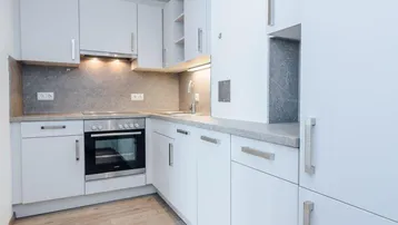 Moderne Einbauküche in Weiß mit integrierten Geräten, hellem Laminatboden und Deckenspots.