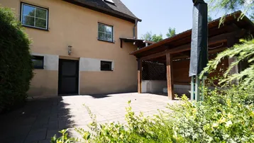 Gepflasterte Terrasse mit Holzüberdachung und Blick auf die grüne Umgebung des Hauses.