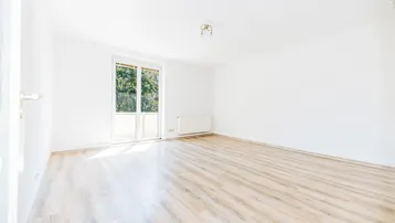 Leeres, helles Wohnzimmer mit Laminatboden und Zugang zu einem französischen Balkon.