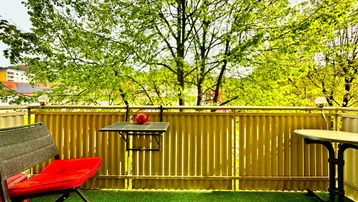 Heller Balkon mit Kunstrasen, Gartenmöbeln und Blick ins Grüne.