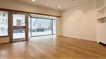 Heller, leerer Gewerberaum mit großen Schaufenstern zur Straße und einem schönen Holzfußboden.