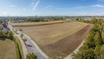 Luftaufnahme eines großen unbebauten Grundstücks mit angrenzender Wohnbebauung und Fernblick auf die Stadt.