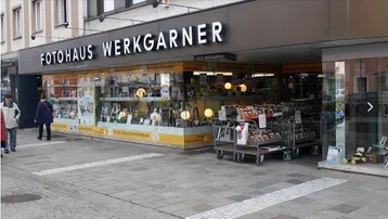 Ansicht der Ladenfront des Fotohauses Werkgartner mit großen Schaufenstern und Passanten auf dem Bürgersteig.