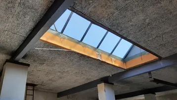 Großer, unfertiger Innenraum mit sichtbaren Deckenbalken und einem Oberlicht, das Tageslicht hereinlässt.