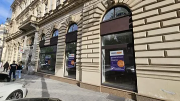 Die Fassade des Gebäudes zeigt große Bogenfenster und eine strukturierte Oberfläche mit Mietanzeigen.