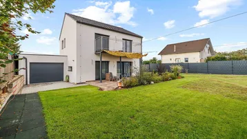 Modernes Einfamilienhaus mit großem Garten, Terrasse und Balkon, umgeben von viel Grün.