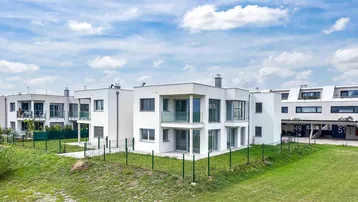 Moderne weiße Wohngebäude mit großen Fenstern und Balkonen, umgeben von Grünflächen unter blauem Himmel.