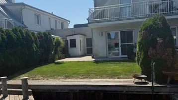 Hinterhof mit Rasenfläche, Holzsteg und Blick auf das Wasser.