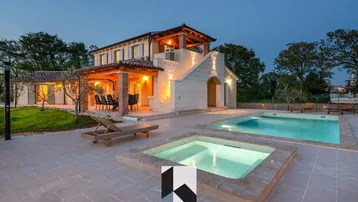 Beleuchtete Villa bei Nacht mit großem Poolbereich und Whirlpool im Freien.