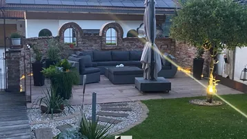 Große Terrasse mit Lounge-Möbeln, Garten und Solaranlage auf dem Dach.