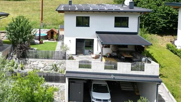 Modernes Einfamilienhaus mit Photovoltaikanlage, Carport, großer Terrasse und Garten mit kleinem Pool.