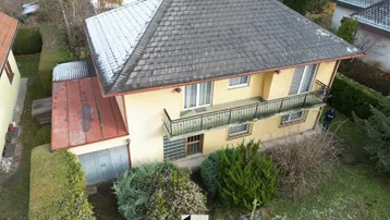 Luftaufnahme eines Einfamilienhauses mit Satteldach, Balkon und Gartenbereich im Winter.