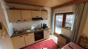 Kleine Küche mit hellen Schränken, Holzbalkendecke und Zugang zu einem Außenbereich.