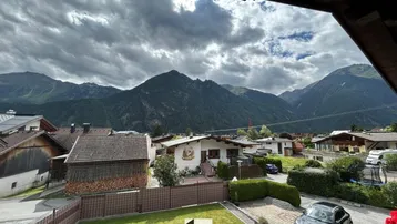 Blick von der Unterkunft auf die umliegende Berglandschaft und das Dorf mit Gärten.