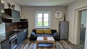 Moderne Küche mit dunklen Schränken, Holzboden und einem kleinen Wohnbereich mit Sofa.